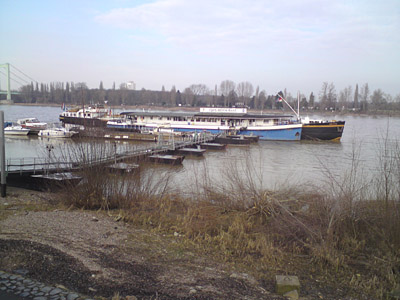 Bootshaus mit Jachtenstegen. Dahinter liegt ein Binnenschiff.
