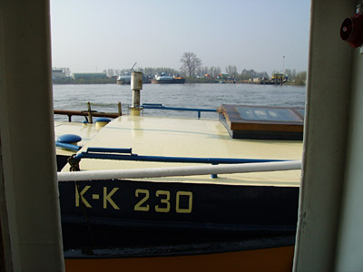 Blick aus der Binnenschiffwohnung, über das Deck vom geschleppten Boot auf einen Binnenhafen.