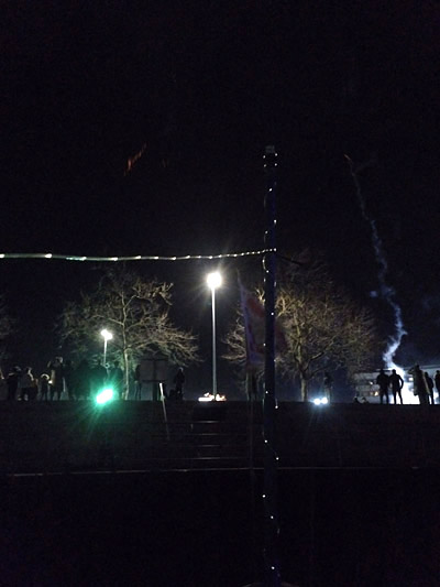 Mast mit Lichtern vor Menschen auf Ufertreppe, Silvesterrauch